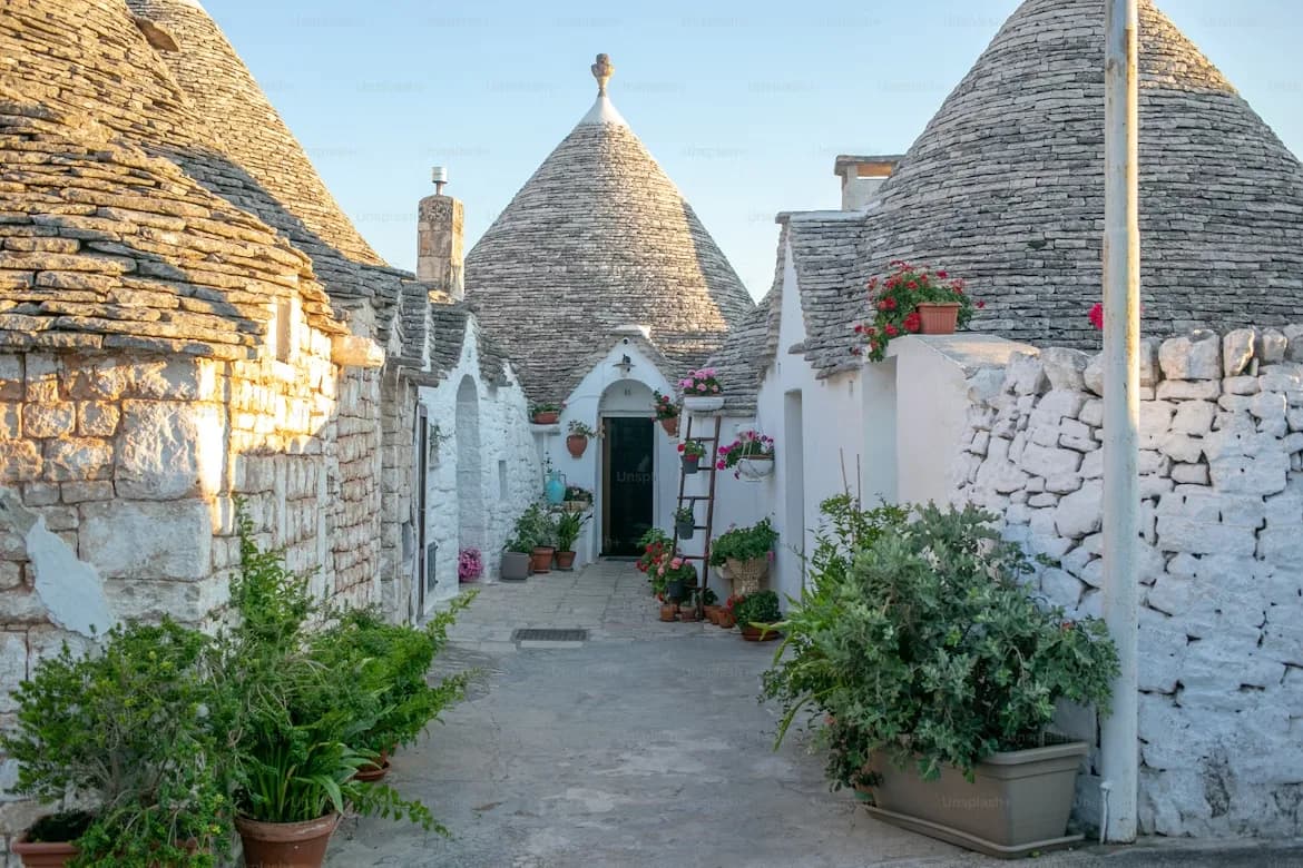 Traditional Trulli houses, with their conical stone roofs and whitewashed walls, are nestled along a narrow, quiet street.