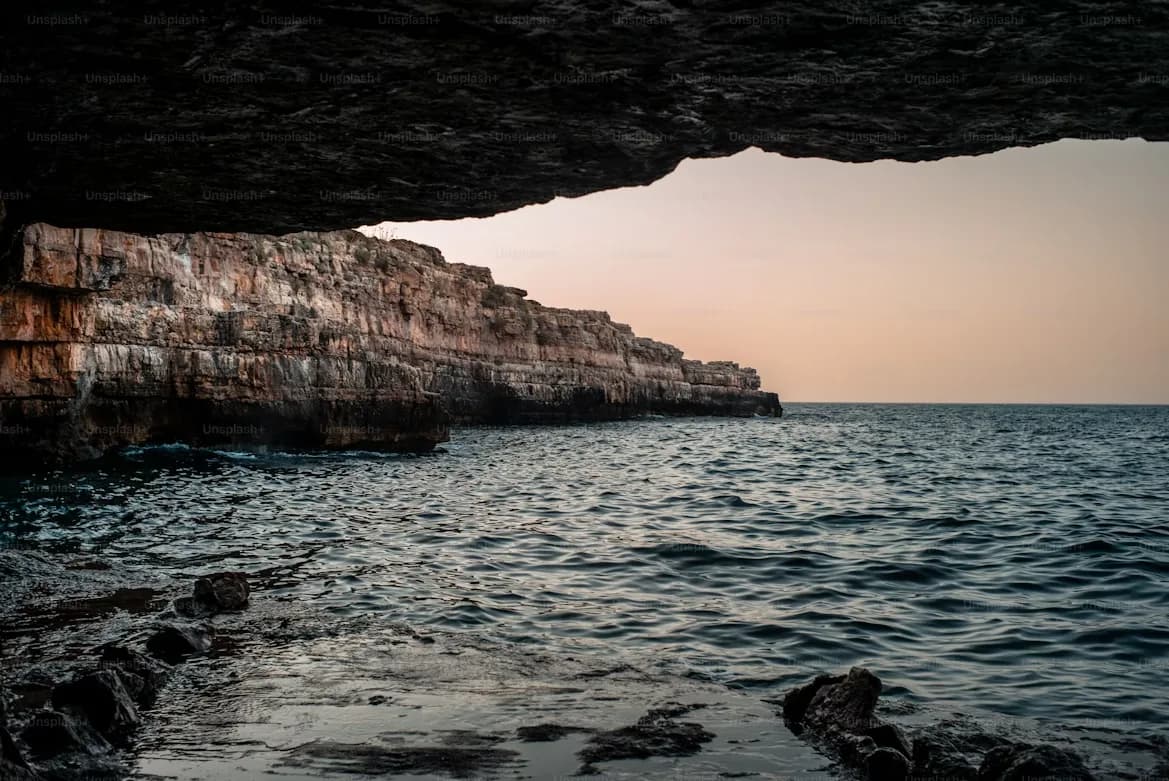 The entrance to a sea cave reveals the vast, open ocean and a dramatic coastline.