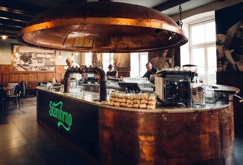 The warm and inviting interior of a traditional brewery features a large, central copper bar and a few people enjoying a drink.