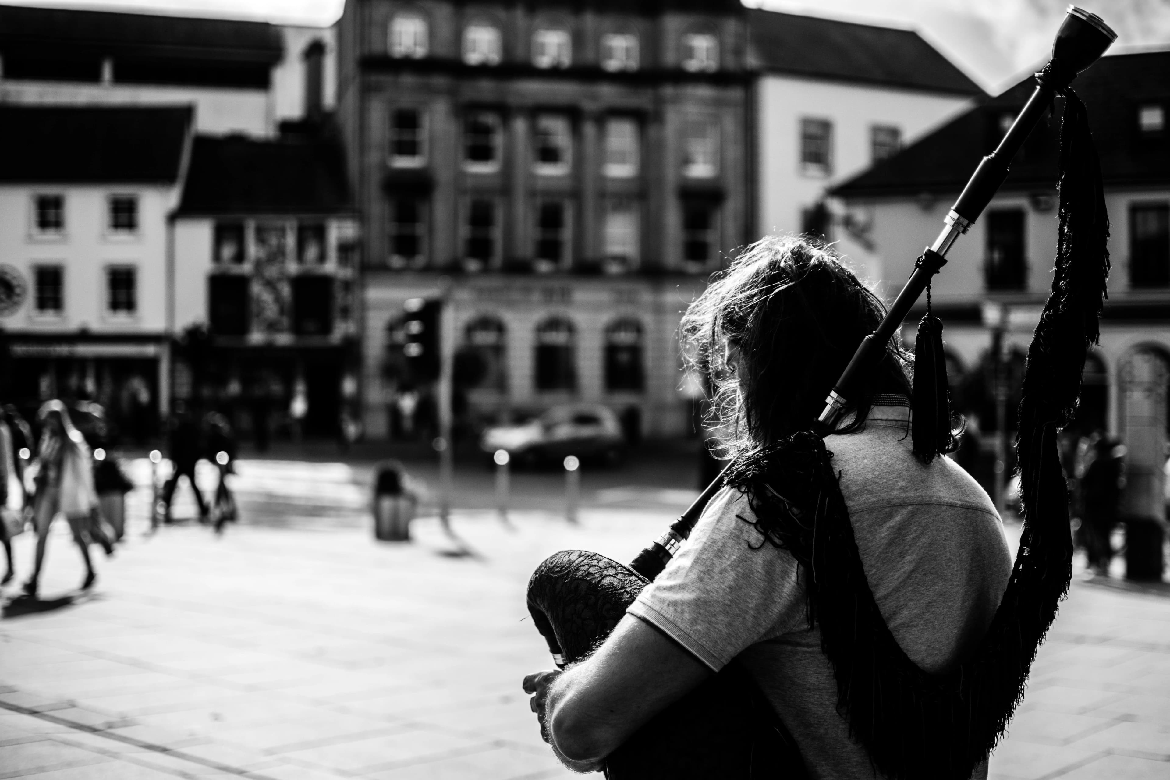 A person is seen from the back, playing the bagpipes in the middle of a city square, adding to the cultural ambiance.