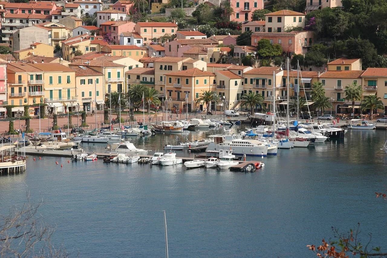 The bustling harbor of Portoferraio is filled with boats and yachts, with the traditional pastel-colored houses of the town built into the hillside.