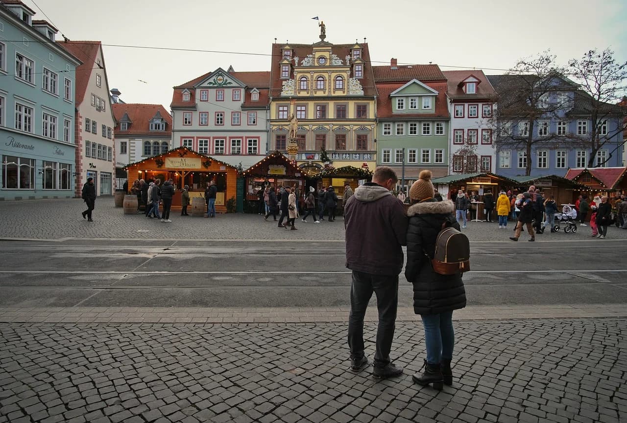 People browse stalls at a Christmas market in the historic Domplatz, with the beautiful gabled buildings of Erfurt's Old Town in the background.