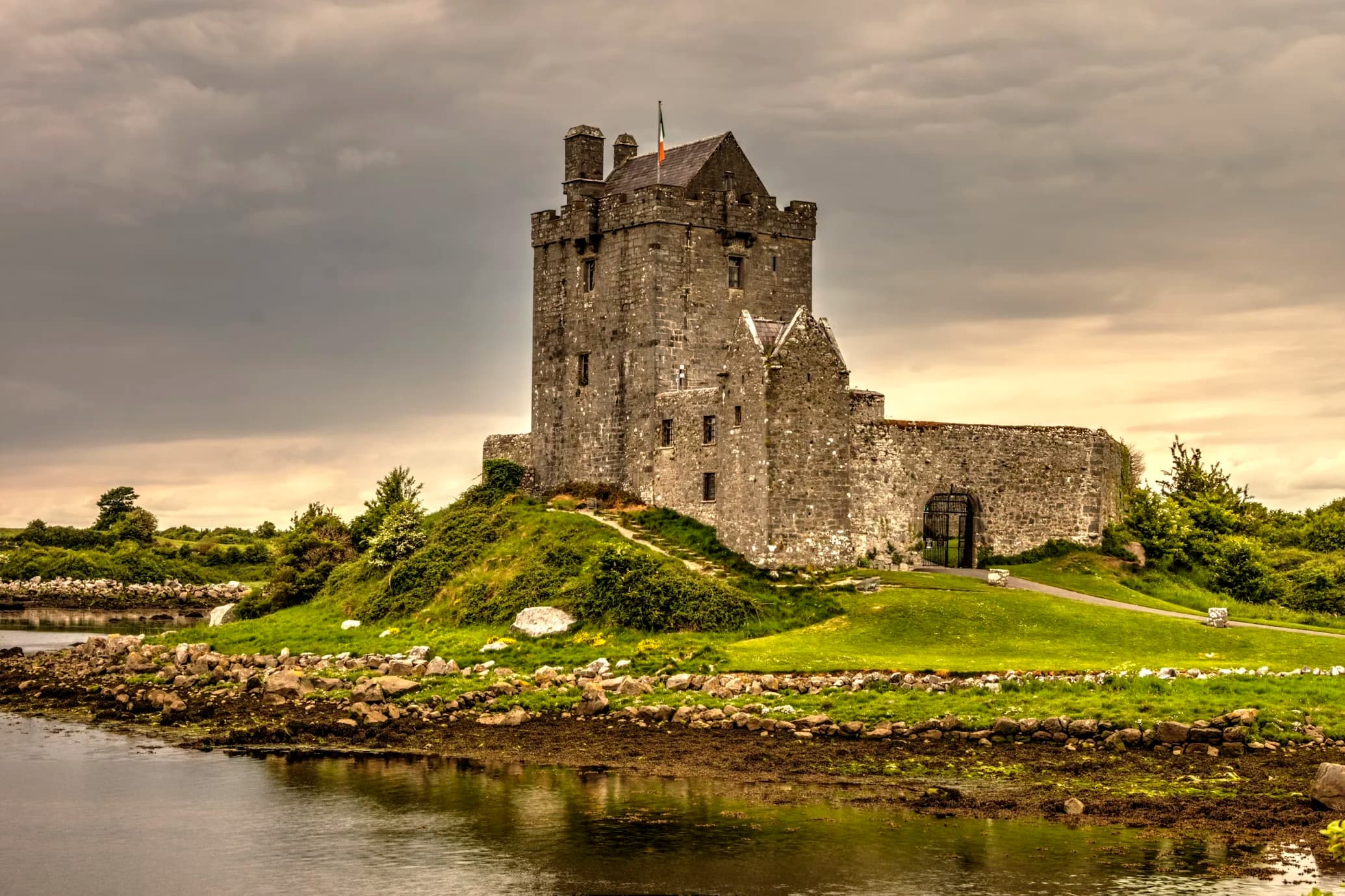 Dunguaire Castle, a well-preserved medieval tower house, stands on a small island surrounded by green grass and a tranquil body of water.