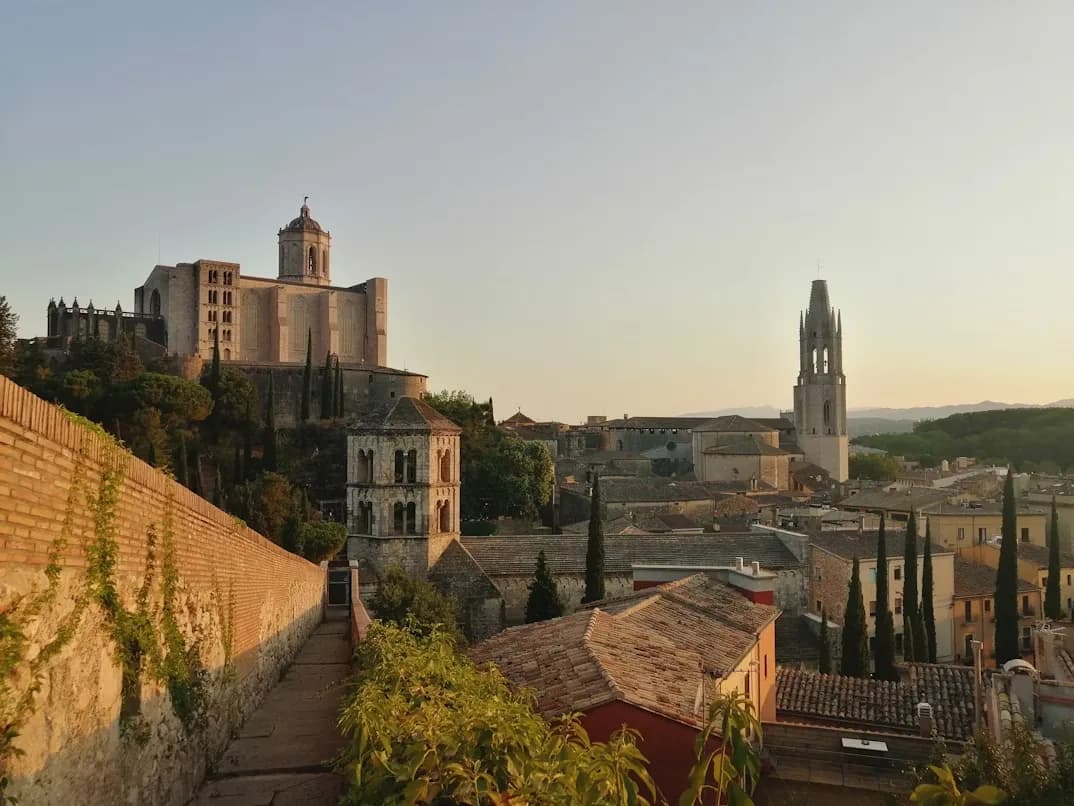 The Church of Sant Feliu stands on a hill above the city, with a prominent bell tower and a winding path leading up to it.