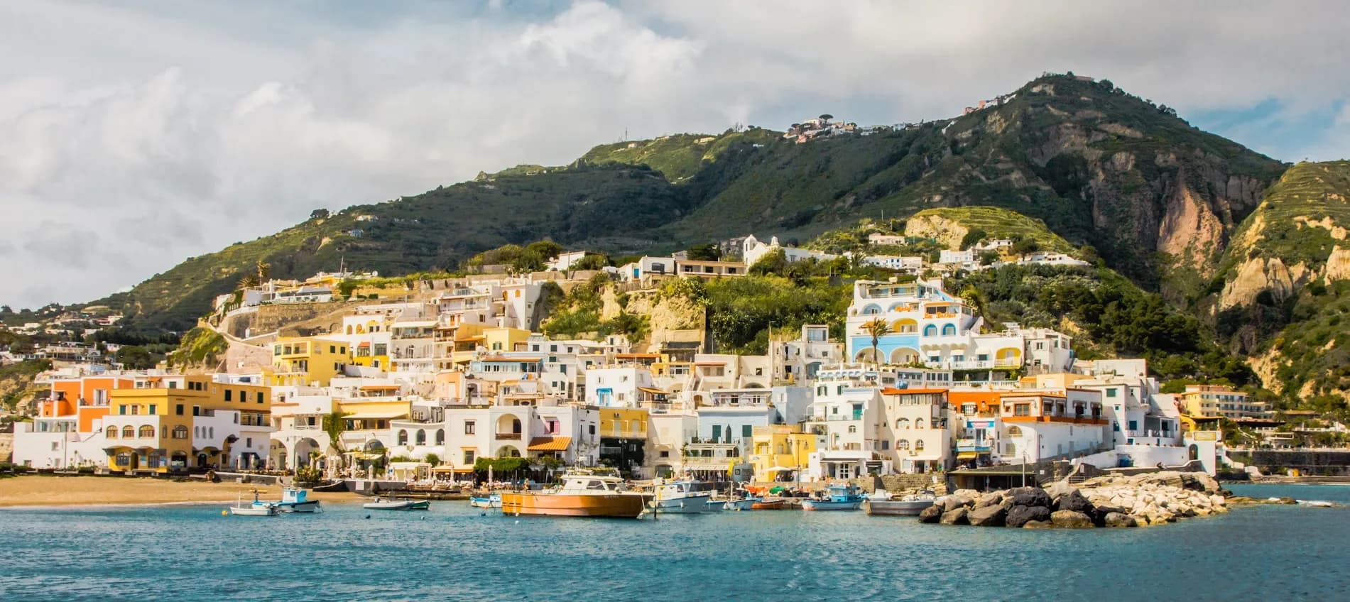 Colorful traditional houses are built into the hillside of Ischia, reflecting on the tranquil waters of the harbor.
