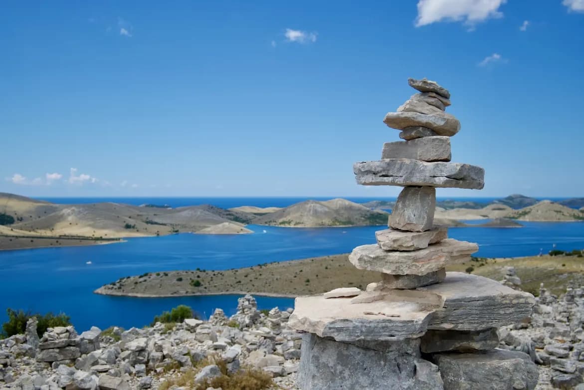 A stack of stones provides a foreground for a panoramic view of the numerous islands and blue waters of Kornati National Park.