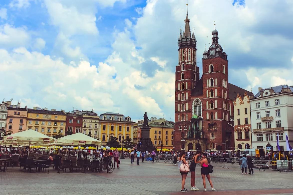 Tourists and locals gather in Krakow's Old Town square, with the imposing towers of St. Mary's Basilica dominating the skyline.