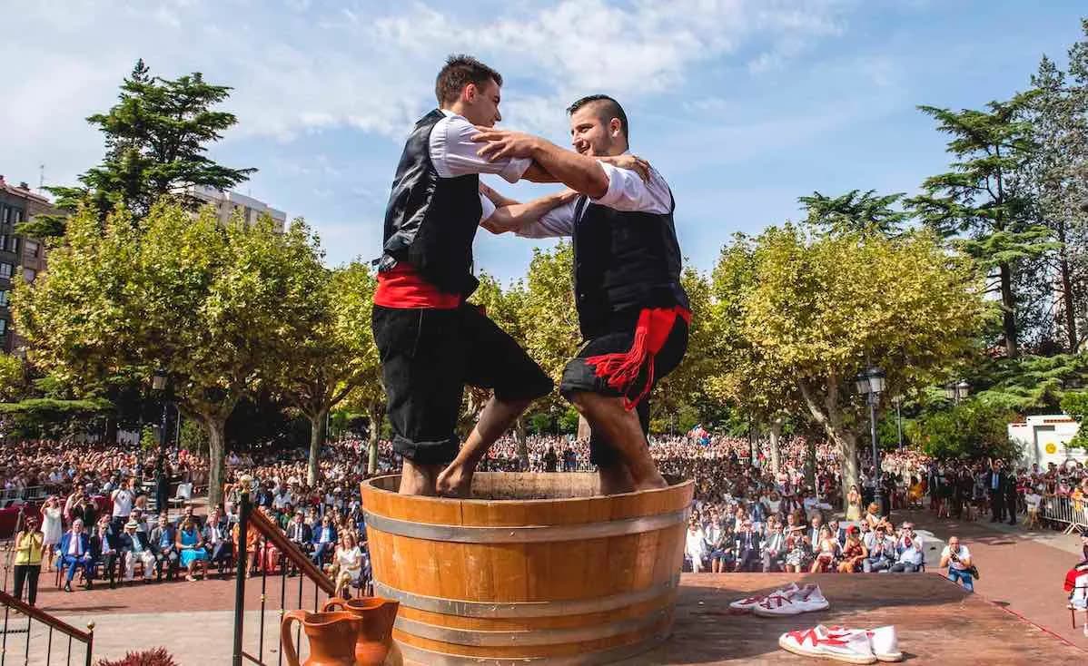 Two men stomp grapes in a large wooden barrel, a traditional part of the grape harvest festival in Logroño.
