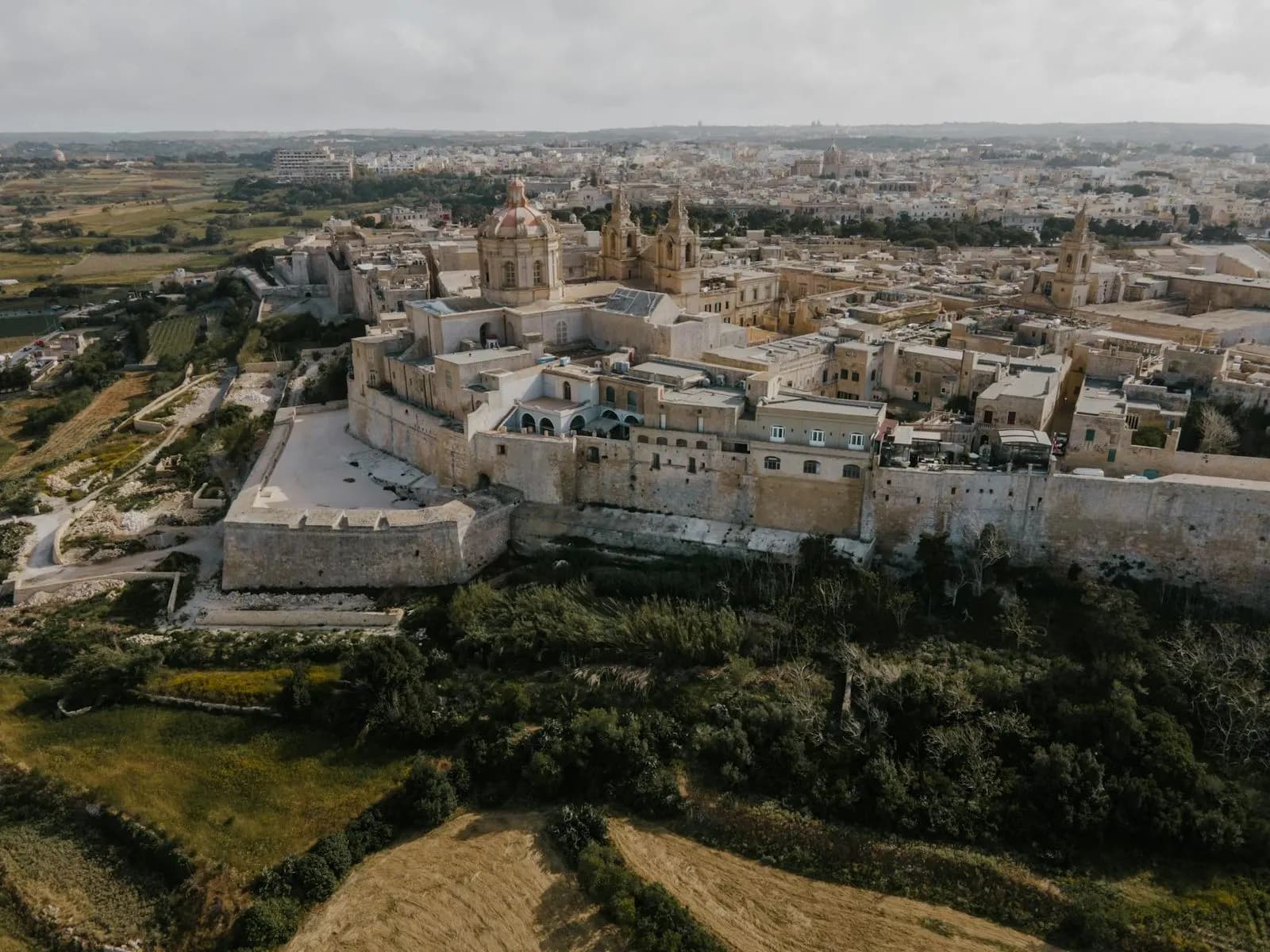 An aerial view captures the historic fortified city of Mdina, with its bell towers and cathedrals.