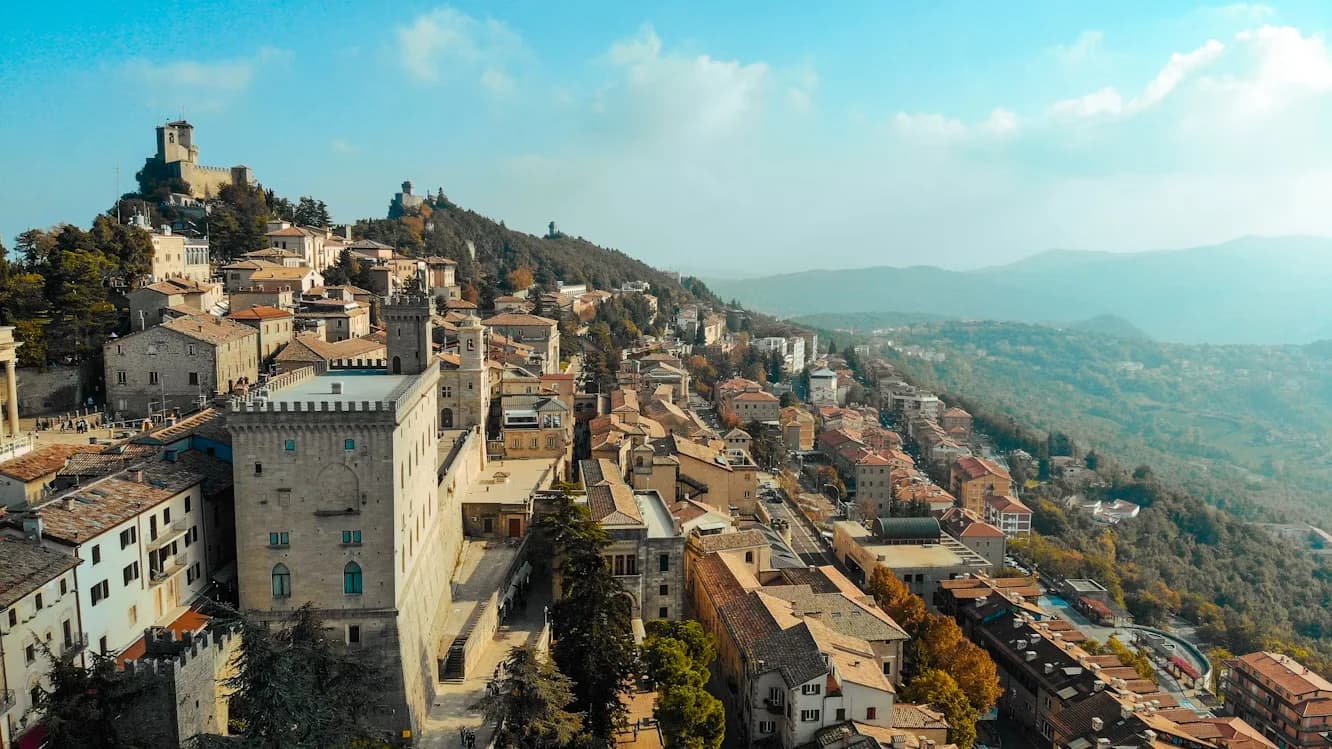 A panoramic view of the historic town of San Marino shows a cluster of buildings on a hillside, with a fortress on top.