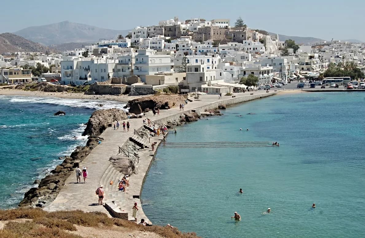 A long stone walkway leads to the historic Temple of Apollo, with the white-washed buildings of the city in the background.