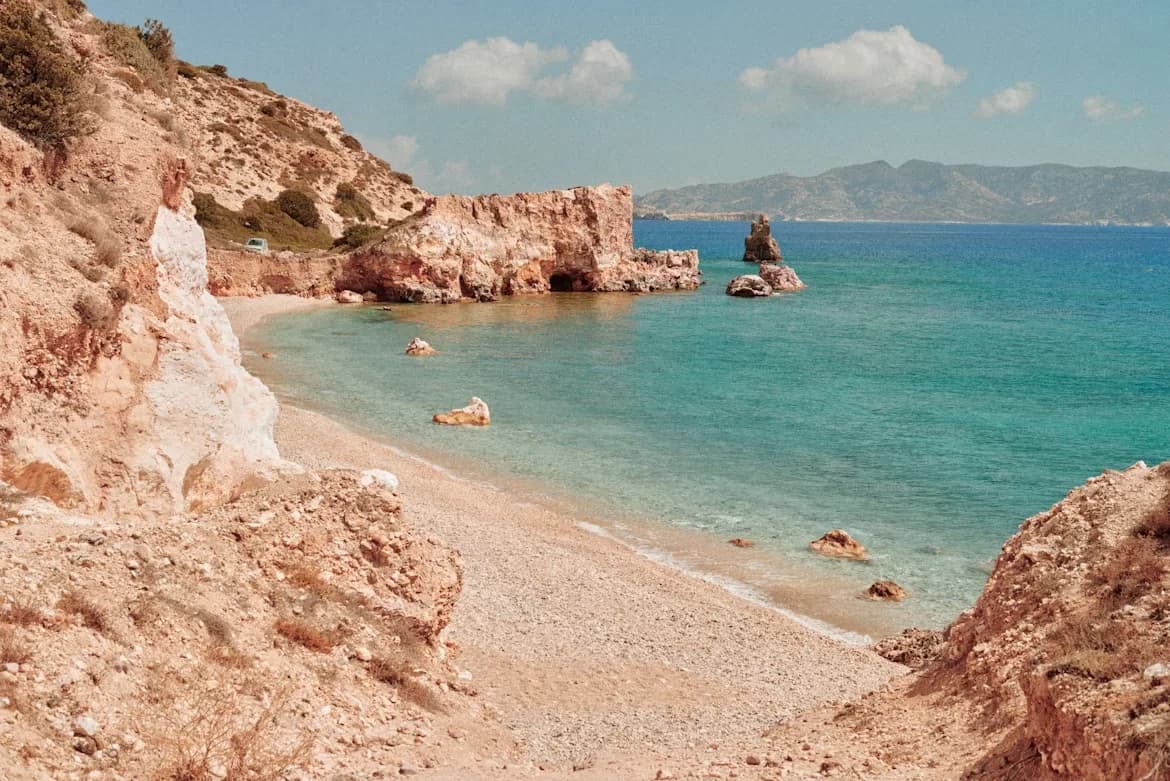 A secluded, rocky beach with crystal-clear turquoise water is nestled between two rocky hillsides.