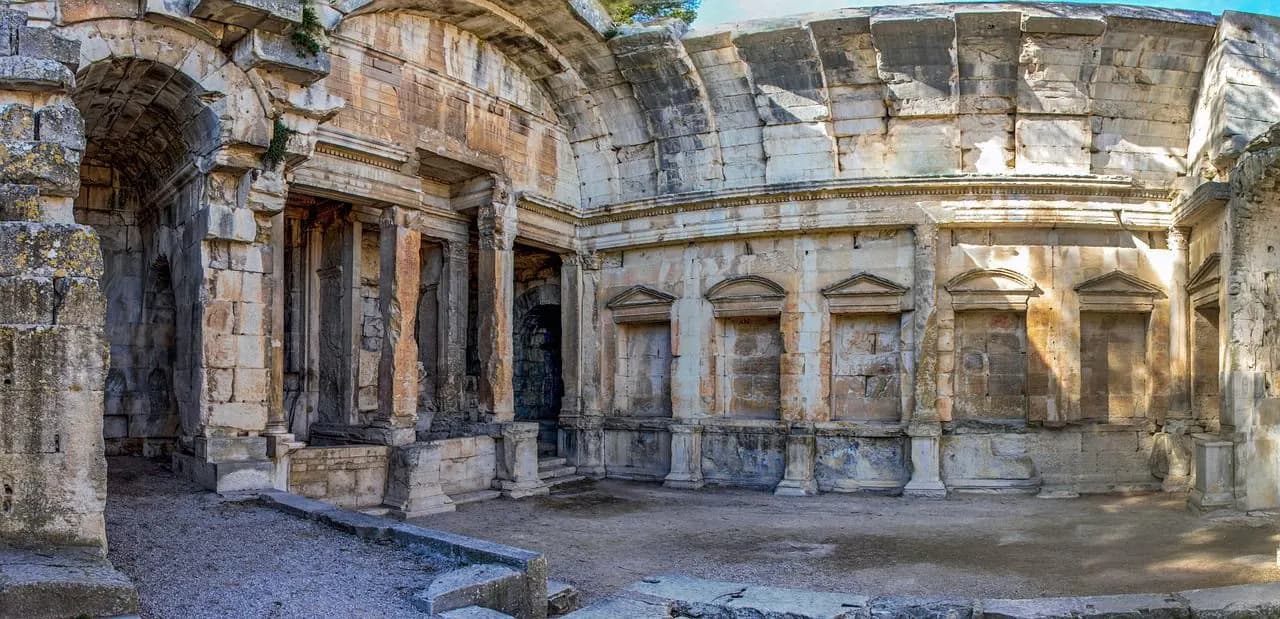 The ruins of a historic Roman building, with its grand archways and columns, stands in a sunlit courtyard.