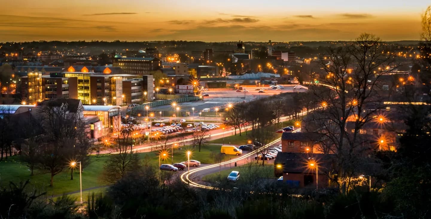 The illuminated Norwich city skyline glows at dusk, with the lights of the buildings creating a beautiful urban landscape.