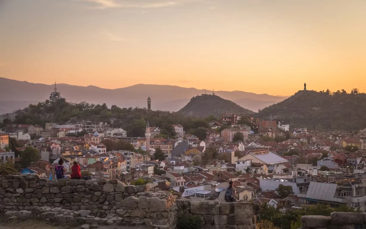 A wide-angle view of the Plovdiv Old Town shows the rooftops and hills in the background, with the city's landmarks glowing at sunset.
