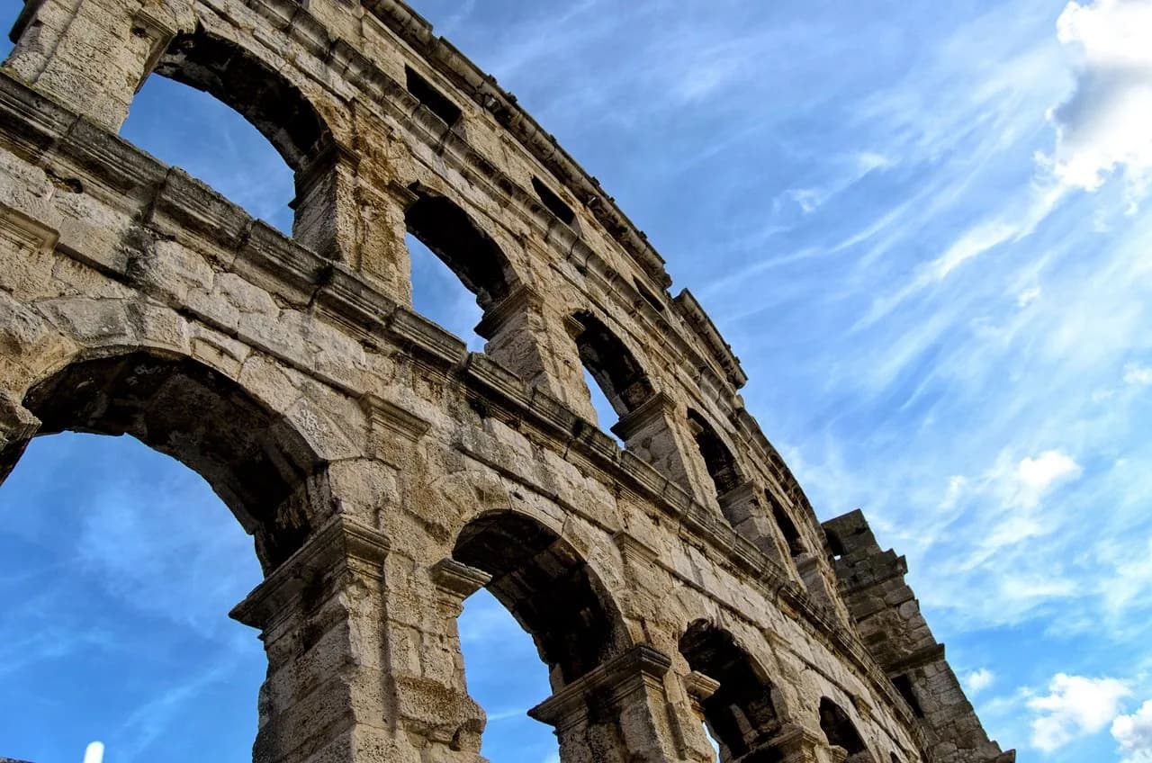 The towering arches of the Pula Arena, a well-preserved Roman amphitheater, stand majestically against a bright blue sky.