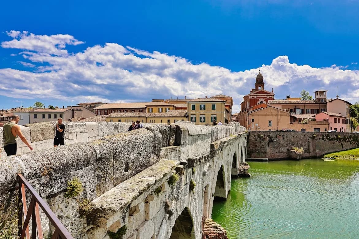People walk along the ancient Tiberius Bridge, a Roman landmark that crosses the Marecchia River in Rimini.