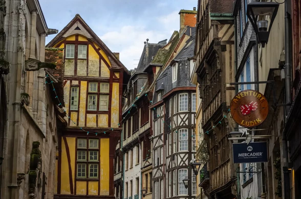 A narrow, historic street is lined with traditional half-timbered houses and small shops.