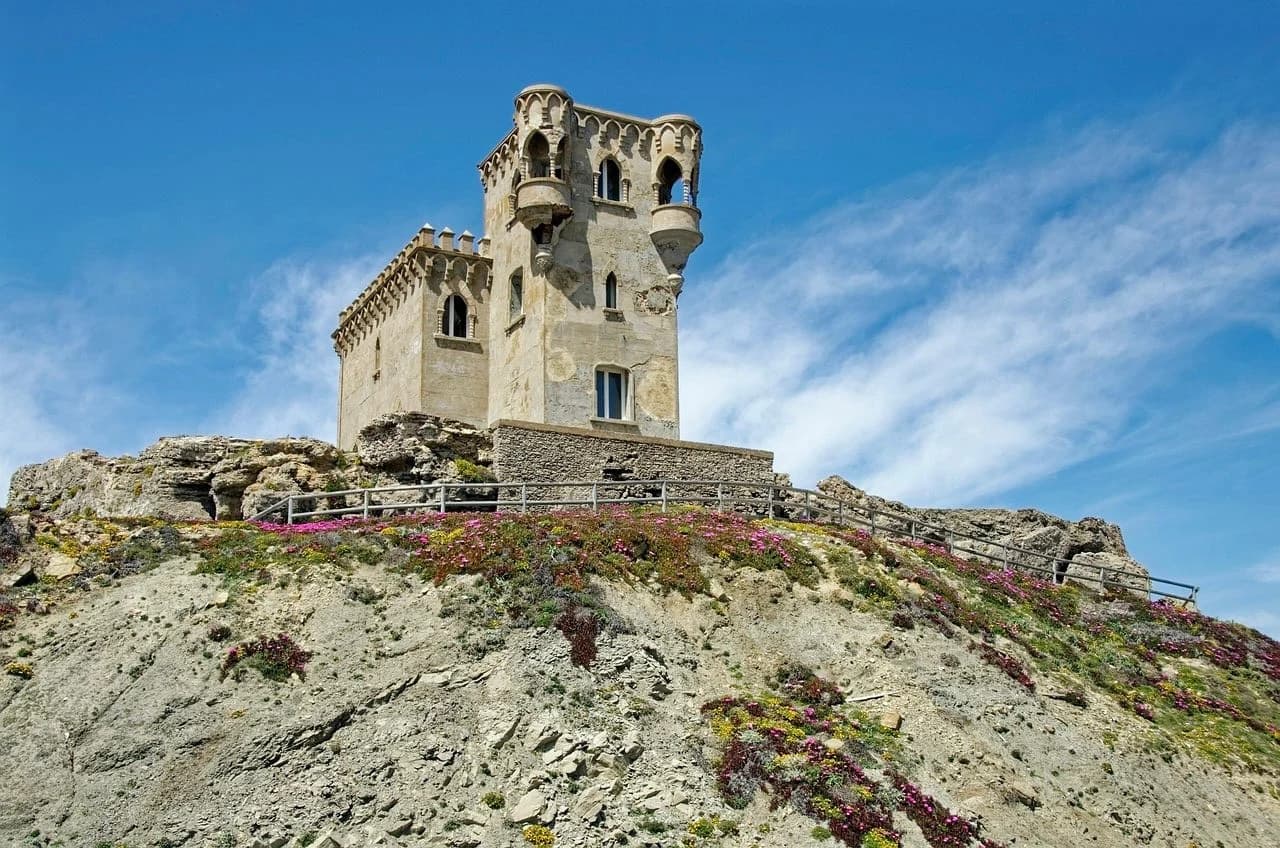 A row of colorful kites floats in the air, with a wide, sandy beach and the sea stretching to the horizon.
