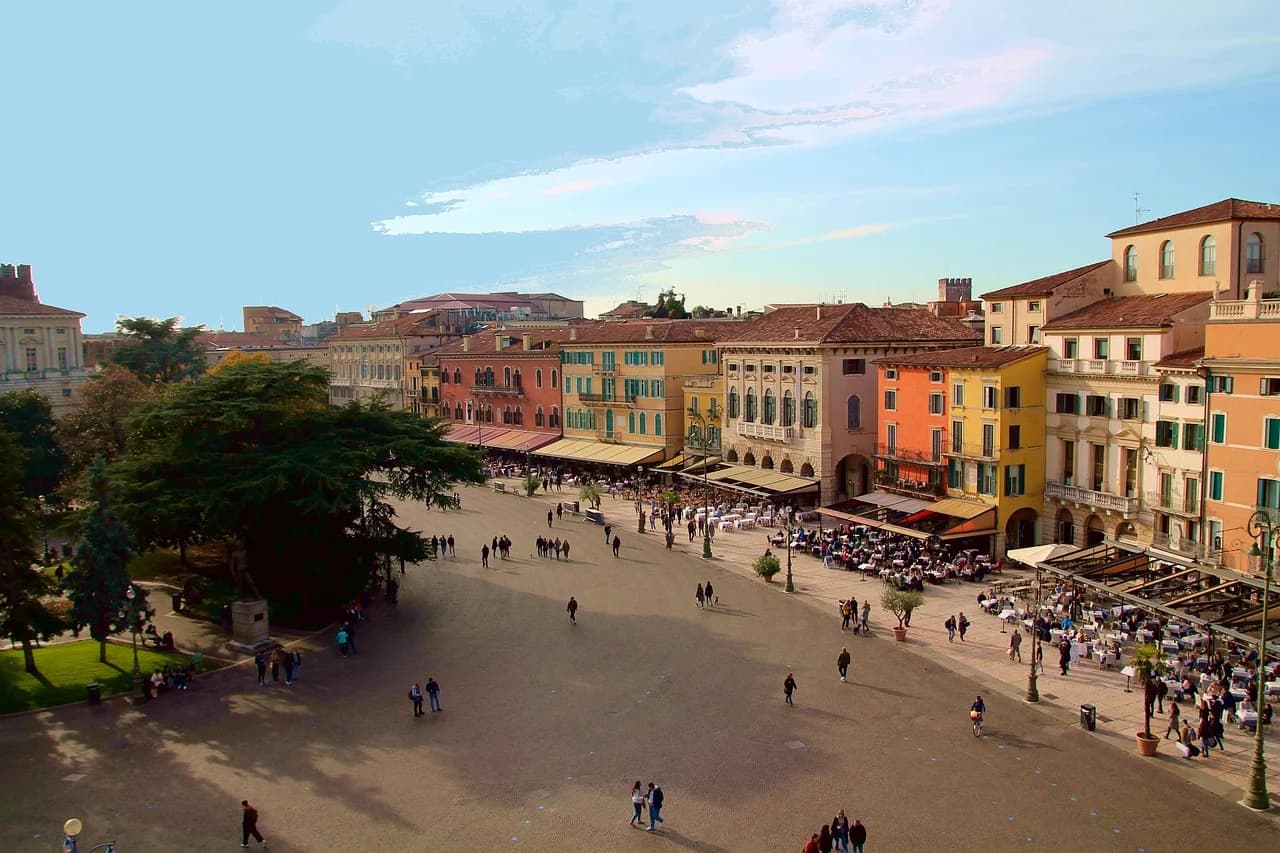 The historic Ponte Scaligero, a medieval stone bridge, spans the Adige River, with a view of the city and the mountains.